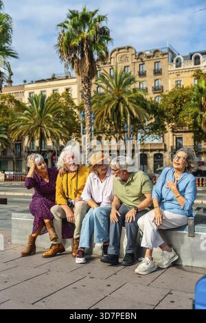 Eine Gruppe glücklicher Seniorenfreunde genießt ihren Stadturlaub, sitzt draußen und lacht zusammen unter den Palmen, feiert Freundschaft und ac Stockfoto