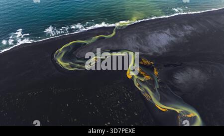 Aus der Vogelperspektive auf einen Serpentinfluss, der sich durch schwarzen vulkanischen Sand schlängelt, dessen Wasser in Ocker- und Jadetönen sprudelt, während er auf das türkisfarbene Meer trifft, HVO Stockfoto