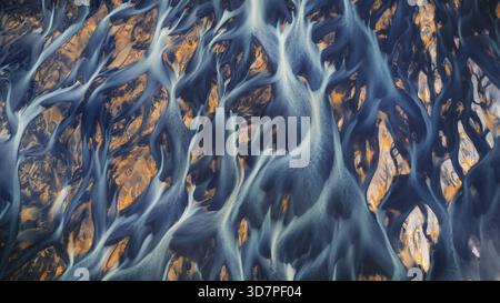 Aus der Vogelperspektive ziehen sich Gletscherflüsse durch die Landschaft und bilden ein faszinierendes Netz aus eisblauen Adern gegen die warmen Erdtöne Hvolsvollu Stockfoto