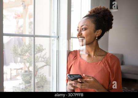 Glückliche, traumhafte afrikanische Frau, die aus dem Fenster schaut Stockfoto