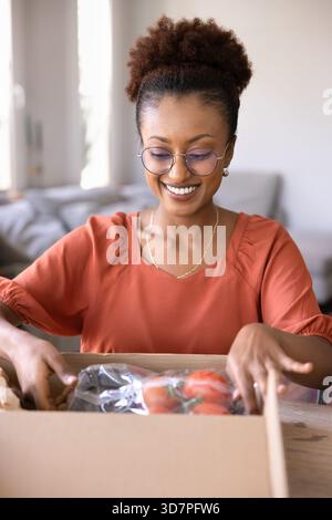 Glückliche junge afroamerikanische Supermarktkundschaft, die den Karton auspackt Stockfoto