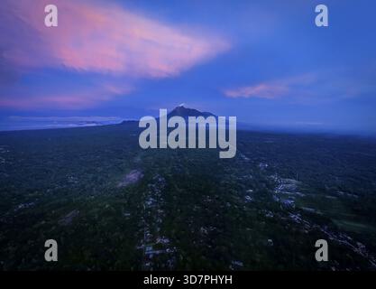 Aus einem dichten Wald erhebt sich ein majestätischer Berg aus der Vogelperspektive unter einem Himmel, der in Rosa- und Blautönen in der Abenddämmerung gemalt ist, Yogyakarta, Daerah Istimewa Yogya Stockfoto