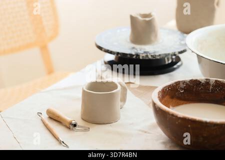 Tonbecher und Töpferwerkzeuge auf dem Tisch im Heimstudio, Nahaufnahme Stockfoto