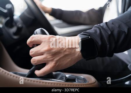 Nahaufnahme eines Fahrers, der den Schalthebel bewegt, während er eine Smartwatch trägt, und hebt Kontrolle, Technologie und modernen Fahrstil in hervor Stockfoto