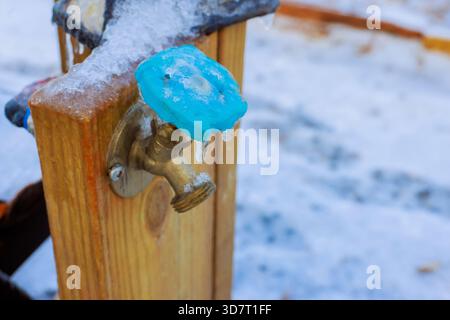 Eiskalter Wasserhahn auf Holzpfosten zeigt Anzeichen von Frost in verschneite Umgebung im Winter. Stockfoto