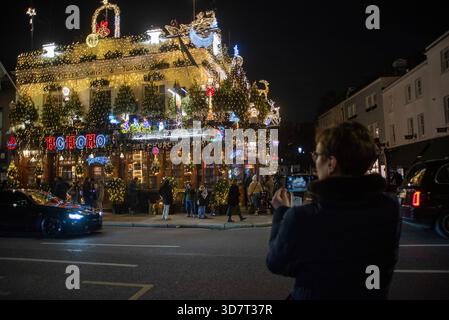 London, Großbritannien. November 2025. Ein Tourist macht ein Foto im Churchill Arms. Das Churchill Arms befindet sich in der Nähe der Notting Hill Gate Station. Es ist der weihnachtlichste Pub seit über 30 Jahren. In diesem Jahr wurden fast 100 Nadelbäume und 135000 Lichter verwendet, um den Pub draußen zu dekorieren. Quelle: SOPA Images Limited/Alamy Live News Stockfoto