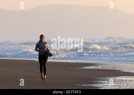 Frau, die barfuß am Ocean Beach in San Francisco bei Sonnenuntergang läuft Stockfoto