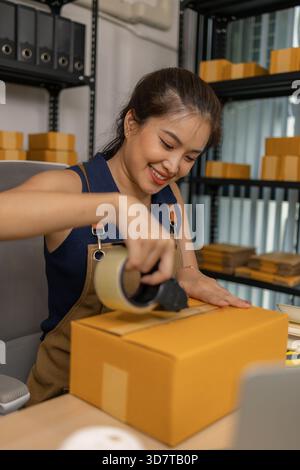 Die junge Unternehmerin versiegelt das Paket sorgfältig mit Klebeband, bereitet Warenbestellungen vor, verwaltet den Versand und die Lieferung für sie erfolgreich online Stockfoto