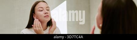 Junge kaukasische Frau, die Skincare Cream im Morgenalltag aufträgt Stockfoto