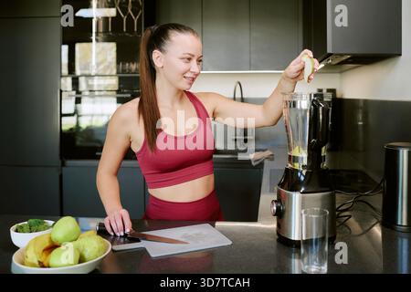 Junge kaukasische Frau, die gesunden Morgen-Smoothie in der modernen Küche zubereitet Stockfoto