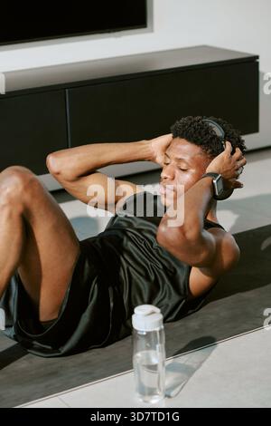 Junger erwachsener Schwarzer Mann, der Musik hört, während er Crunches im Morgenlicht macht Stockfoto