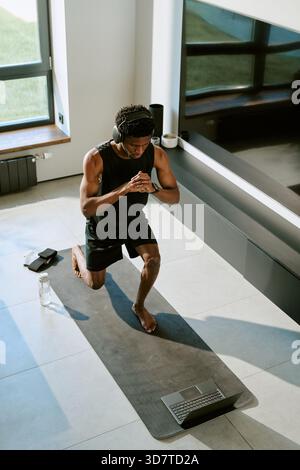 Junger Erwachsener Schwarzer Mann, der während des virtuellen Morning Workouts auf Yogamatte trainiert Stockfoto