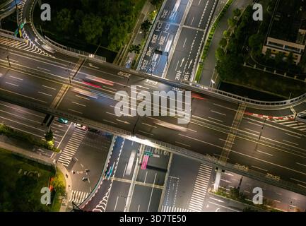 Luftaufnahme einer befahrenen Autobahnkreuzung bei Nacht in einem Stadtgebiet mit Lichtspuren. Stockfoto