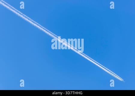 Ein Flugzeug, das gegen den blauen Himmel fliegt, hinterlässt eine lange, vierfache, weiße Spur auf der Diagonale Stockfoto