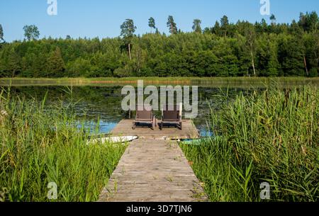Zwei Liegestühle und Boote mit Blick auf einen See in der Nähe von Saldus in der Region Kurland in Lettland. Stockfoto