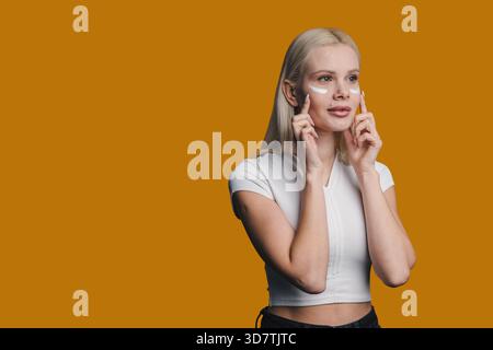 Hellhäutige Frau mit fröhlichem Ausdruck, enthusiastische Dame in weiß, die Gesichtstechniken demonstriert Stockfoto