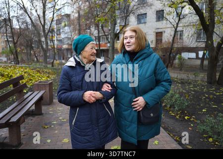 Zwei ältere Damen, Mutter und Tochter, laufen an einem Herbsttag im Park, reden und lachen. Stockfoto