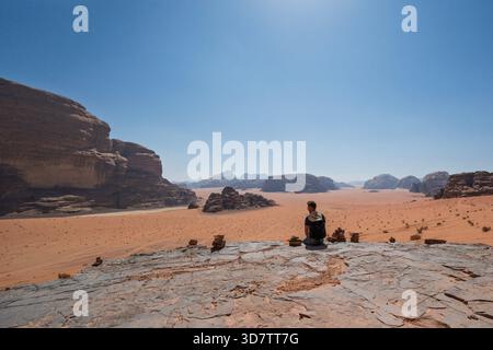 Touristen sitzen auf felsigem Felsvorsprung mit steinhügeln in Wadi Rum, Jordanien Stockfoto