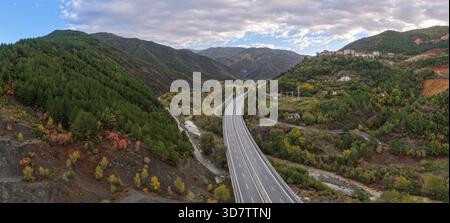 Aus der Vogelperspektive auf Reps im Norden Albaniens, mit Häusern am Hügel und der Autobahn A1 Rruga e Kombit, die durch die üppige Berglandschaft führt. Stockfoto