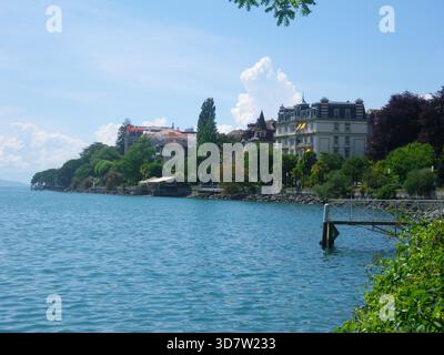 Ein wunderschöner Blick von einem der felsigen Wege mit Blick auf den Genfer See, der die ruhige Stadt und die grüne Natur auf der gegenüberliegenden Uferseite zeigt. Stockfoto