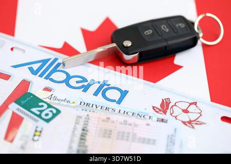 Alberta canadian Autokennzeichen und Zündschlüssel auf der Flagge von Kanada Nahaufnahme. Führerschein- und Zulassungskonzept Stockfoto