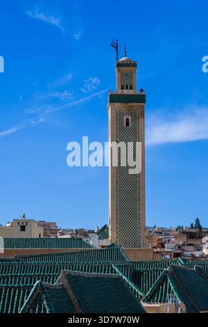 Hoher Minarettturm, der sich über den Dächern der Stadt unter einem hellblauen Himmel erhebt. Fès, Fès-Meknes, Nordmarokko Stockfoto