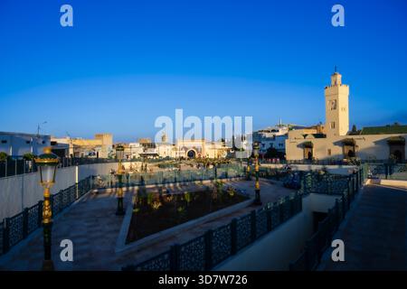 Ein pulsierender Stadtplatz mit traditioneller Architektur unter einem klaren blauen Himmel bei Sonnenuntergang. Fès, Fès-Meknes, Nordmarokko Stockfoto