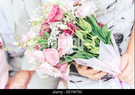 Zartes rosafarbenes Brautstrauß in den Händen während eines Hochzeitsmoments in Lettland mit zarten Blumen und Grün. Stockfoto