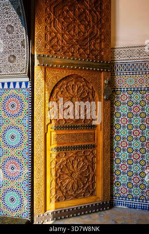 Komplizierte Holztür mit kunstvollen Schnitzereien und farbenfrohen Mosaikfliesen in sattem Detail. Marrakesch, Marokko Stockfoto