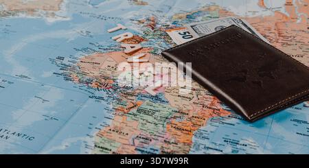 Die farbige Karte zeigt verschiedene Länder, während Reisemeldungen in der Nähe sitzen, neben einem braunen Pass und einem 50-Dollar-Schein, was Pläne für eine bevorstehende Reise vorschlägt Stockfoto