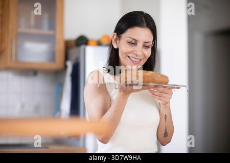 Frau lächelt, während sie einen frisch gebackenen Brotlaib in einer modernen Küche in Deutschland hält Stockfoto