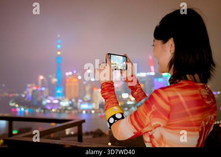 Frau, die nachts mit einem Smartphone aus einer hohen Perspektive eine Skyline der Stadt festnimmt. Shanghai, China Stockfoto