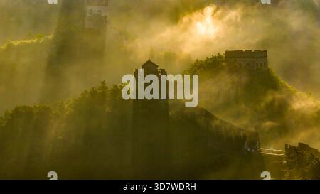 Morgennebel und Sonnenstrahlen beleuchten die alten Wachtürme der Chinesischen Mauer in Jinshanling, Provinz Hebei, China. Stockfoto