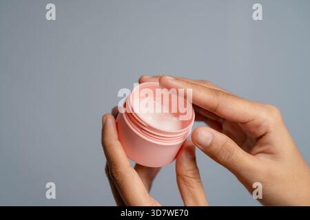 Nahaufnahme der Hände, die Ein rosafarbenes offenes Glas Creme mit Einem hellrosa Farbton halten Stockfoto