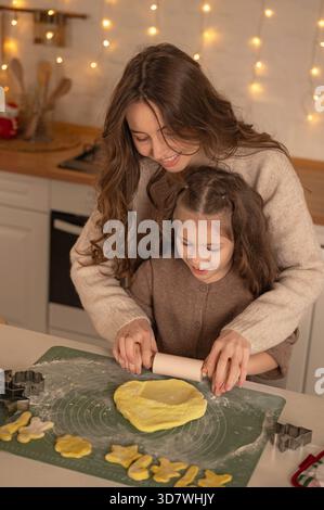 Mutter und Tochter rollender Keksenteig in der gemütlichen Weihnachtsküche Stockfoto