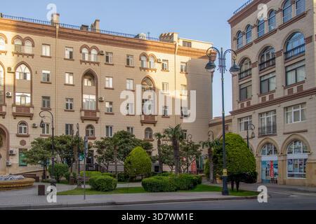 Baku, Aserbaidschan. Wunderschönes Gebäude in der Inshaatchilar Avenue mit einzigartigen architektonischen Stilen. Üppig grüne Bäume verstärken die lebhafte Atmosphäre o Stockfoto