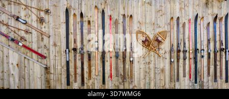 Eine Sammlung antiker Holzskier und traditioneller lederbezogener Schneeschuhe hängt senkrecht an einem rustikalen, alten Holzzaun. Dieses Gerät, Stockfoto