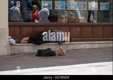 Chania, Kreta, Griechenland - 22. Juni 2025: Ein Mann liegt an einem warmen Tag auf dem Bürgersteig vor einem Geschäft in Chania, Kreta. Stockfoto