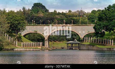 Steinbogenbrücke über den Putrajaya-See mit bezauberndem Pavillon, üppig grünen Hügeln und dekorativen Laternenpfosten. Gelegen in Putrajaya, Kuala Lumpur, Malaysia. Stockfoto