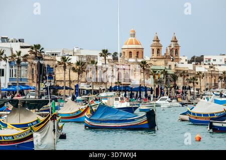 Marsaxlokk, Malta - 13. April 2025: Traditionelle, farbenfrohe maltesische Fischerboote namens Luzzu mit hellblauen, gelben und roten Details, die im malerischen Hafen von Marsaxlokk ankern Stockfoto