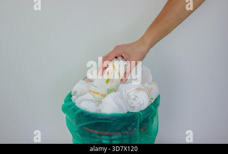 Die Hand einer Frau, die eine gebrauchte Babywindel in einen Mülleimer mit grünem Futter wirft. Stockfoto