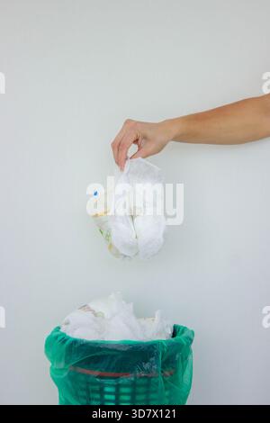 Die Hand einer Frau, die eine gebrauchte Babywindel in einen Mülleimer mit grünem Futter wirft. Stockfoto