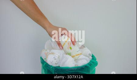 Die Hand einer Frau, die eine gebrauchte Babywindel in einen Mülleimer mit grünem Futter wirft. Stockfoto