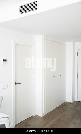 Minimalistischer weißer Korridor mit heller Beleuchtung, Holzboden und sauberen eingebauten Stauflächen Stockfoto