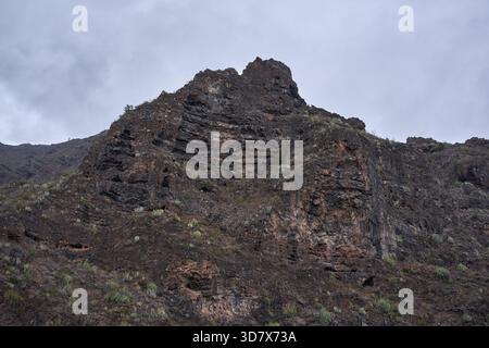 Der mehrschichtige vulkanische Felsgipfel mit dünner, saftiger Vegetation erhebt sich über den Wänden des Canyons in Barranco del Infierno Teneriffa Stockfoto