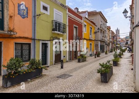 Ein klassischer Blick auf eine kopfsteingepflasterte Straße in Setubals Altstadt, Portugal, mit farbenfrohen Gebäuden, Balkonen und einem Kirchturm in der Ferne. Stockfoto