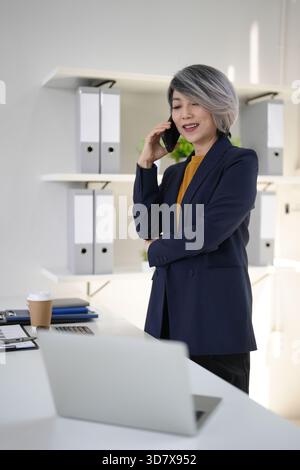 Erfahrene asiatische Führungskräfte kommunizieren über Mobilgeräte an einem modernen Arbeitsplatz und verwalten globale Verbindungen Unternehmensstrategie Stockfoto