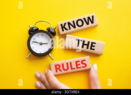 Kennen Sie das Regelsymbol. Holzblöcke mit Worten kennen die Regeln. Geschäftsmann Hand. Schöner gelber Hintergrund mit Wecker. Und kennen Sie die Stockfoto