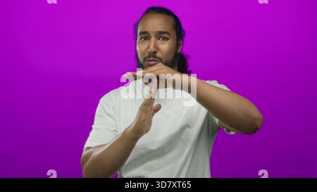 Mann macht Auszeit-Geste mit sichtbaren Händen und Handflächen in weißem T-Shirt im magentafarbenen Studio; halte die Reflexion ernsthaft an. Stockfoto