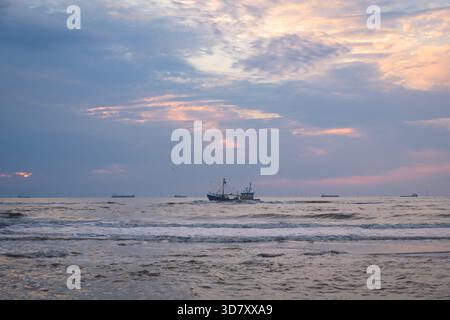 Kleines Fischerboot, das auf der Nordsee unter grauem pastellfarbenen Sonnenuntergang in der Nähe von Scheveningen, Niederlande, driftet Stockfoto
